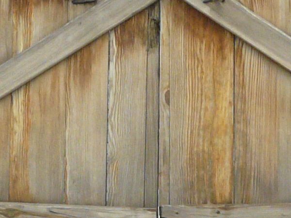 Large wooden gates in light grey tone with arching top and crossbar at center.